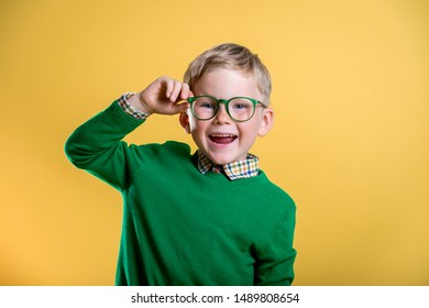 Porträt eines blonden kleinen Jungen in grünem Pullover und Brille. Augenscheintest. Stilvolles Kind, das eine Brille hält und die Kamera anschaut. Sehvermögen, Augenmessung für Schulkinder.Zurück zur Schule.