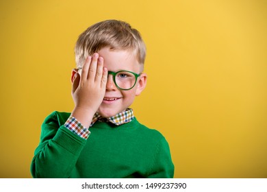 Portrait of blond little boy in green sweater and glasses. Kid at eye sight test. Stylish child holding glasses and looking at camera. Vision, eyesight measurement for school children. Back to school. - Powered by Shutterstock