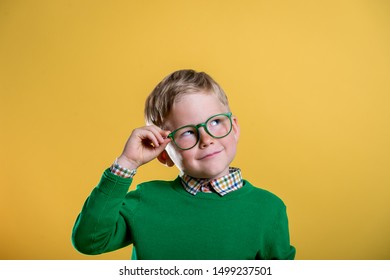 Portrait of blond little boy in green sweater and glasses. Kid at eye sight test. Stylish child holding glasses and looking at camera. Vision, eyesight measurement for school children. Back to school.