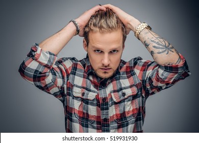 Portrait of a blond male with tattooed arms on his head dressed in a plaid shirt isolated on grey vignette background.