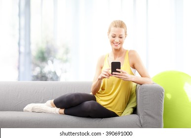 Portrait Of Blond Mature Woman Using Her Mobile Phone While Sitting At Home After Fitness Workout.