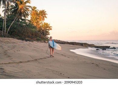 Portrait of blond surfer girl with white surf board in blue ocean pictured from the water in Encuentro beach in Dominican Republic