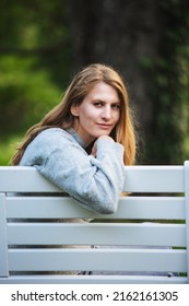 Portrait Of Blond Woman Sitting Outdoors In Park On White Bench