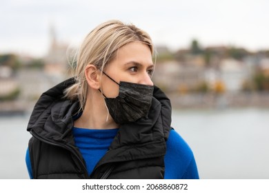 Portrait Of Blonde Caucasian Woman Wearing A Black Surgical Mask Outdoor In The City Because Of Covid-19 Pandemic