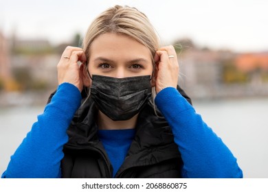 Portrait Of Blonde Caucasian Woman Wearing A Black Surgical Mask Outdoor In The City Because Of Covid-19 Pandemic