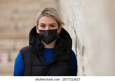 Portrait Of Blonde Caucasian Woman Wearing A Black Surgical Mask Outdoor In The City Because Of Covid-19 Pandemic 