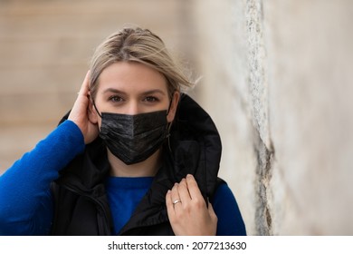 Portrait Of Blonde Caucasian Woman Wearing A Black Surgical Mask Outdoor In The City Because Of Covid-19 Pandemic 