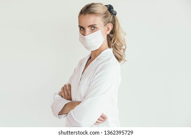 Portrait Of A Blonde Doctor, Nurse Or Scientist Wearing A White Lab Coat And A Mouth Mask.