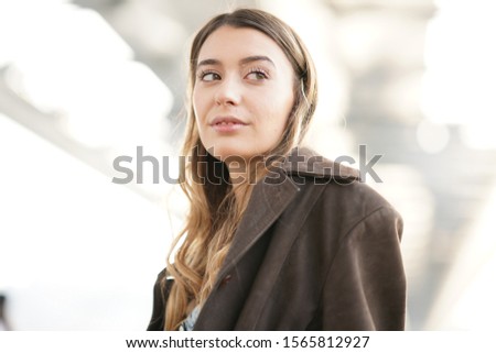 portrait of blonde girl in brown jacket, white shirt under the bridge
