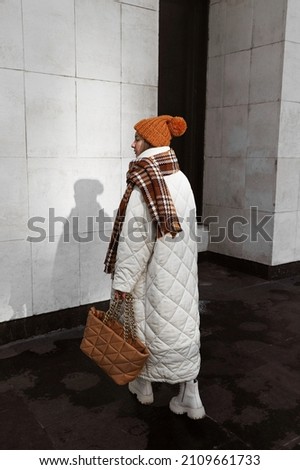 portrait of blonde girl dressed in white quilted down jacket, milky sweater, massive shoes, brown pants, knitted caramel hat scarf and bag, stylish trendy fashion outlook, full length lifestyle model