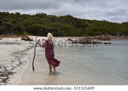 portrait of a blonde girl wearing a long purple dress, wandering along beautiful island shoreline