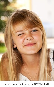 Portrait of a blonde girl winking in a summer's day background