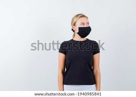 Portrait of blonde lady looking aside in black t-shirt, black mask and looking focused front view 