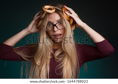 Portrait of a blonde with long hair, in a vinous suit, glasses, on a dark Turquoise Studio background. bunch of bagels on the head. Play The Fool