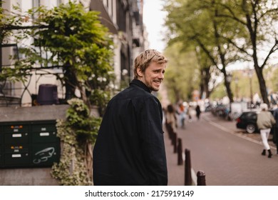 Portrait Of Blonde Man Wear Black Shirt Walk In City Street. Young Man Turned Back And Looked At The Camera. Lifestyle. Man Look Happy And Smiling.