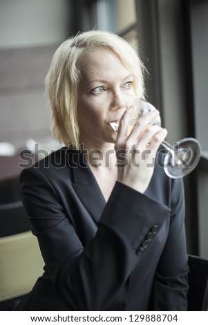 Portrait of a blonde woman drinking a glass of white wine.