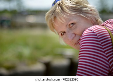 A Portrait Of A Blonde Woman Wearing A White Red Striped Shirt Is Looking Over Her Shoulder Towards You On A Hot And Sunny Day