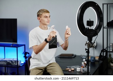 Portrait Of Blonde Young Man Demonstrating Beauty Accessories While Filming Skincare Tutorial At Home, Copy Space