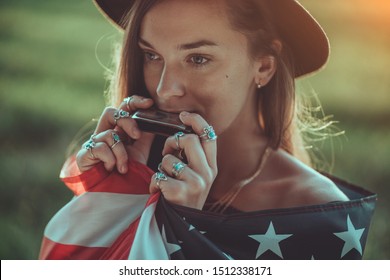 Portrait Of Boho Chic Woman In Hat With American Flag Wearing Silver Rings With Turquoise Stone Playes On Harmonica Outdoors. Jewelry Indie Girl With Hippie Style And Boho Fashion. Travel To America