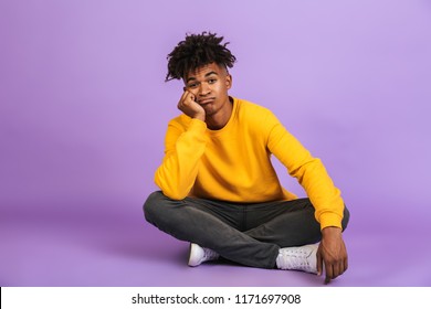 Portrait of bored african american boy sitting on floor with legs crossed and propping his head isolated over violet background - Powered by Shutterstock