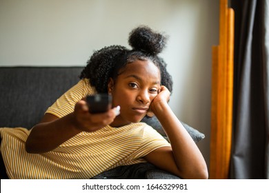 Portrait Of Bored African American Girl On Sofa Pointing Tv Remote Control