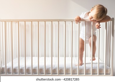Portrait of bored baby standing in crib. Baby boy stand alone in crib. Sad little baby. Lonely baby stay in the crib. Waif child. Loneliness.