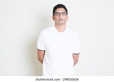 Portrait Of Bored Indian Guy With Serious Face Expression. Asian Man Standing On Plain Background With Shadow And Copy Space. Handsome Male Model.