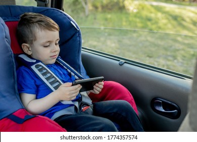 Portrait Of A Bored Little Boy Sitting In A Car Seat. Safety Of Transportation Of Children