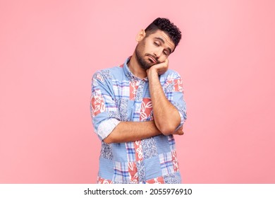 Portrait of bored upset man with beard in blue casual style shirt leaning head on hand laziness and apathy, procrastination, looks sleepy. Indoor studio shot isolated on pink background.