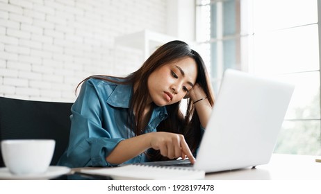 Portrait Of Bored Young Asian Woman Typing Laptop In Office. Freelance Employees Sleeping Lying Head On Hand On Computer Desk Feel Boring. Lifestyle Of Routine Employees Concept.