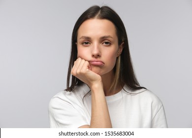 Portrait of bored young woman with head on chin isolated on gray background