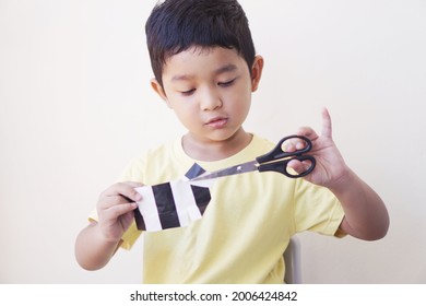 Portrait Of Boy 4-year-old. Asian Kid Holding Scissors Cutting A Paper Make Art Craft Activities Online Learning At Home. Creative Art Concept.                              