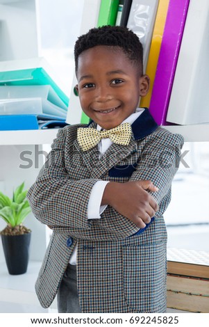 Portrait of boy imitating as businessman standing with arms crossed against self in ffice