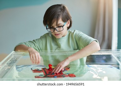 Portrait Of Boy Putting Robo Boat In Water While Experimenting With Technology At Robotics Lab In School