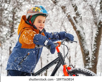 Portrait Of A Boy Riding A Bike In A Winter Park. Active Pastime In Winter After Snowfall