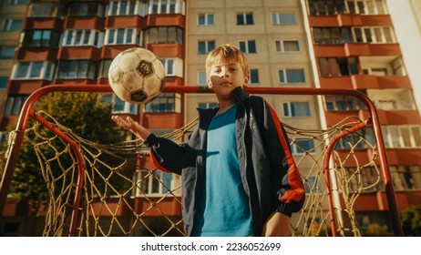 Portrait of a Boy in Sport Clothes Throwing and Catching a Soccer Ball, Standing Next to a Football Gate in the Neighborhood. Young Player Looking at Camera, Smiling. Low Angle Shot. - Powered by Shutterstock