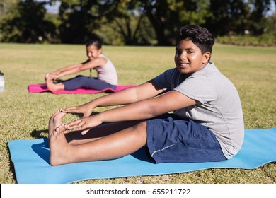 Portrait Of Boy Touching Toes During Yoga Glass On Exercise Mat At Park