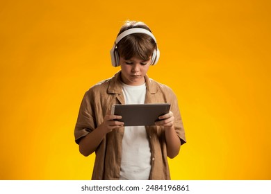 Portrait of boy using tablet and headphones and playing video game over yellow background. Leisure and gadget addiction concept. - Powered by Shutterstock