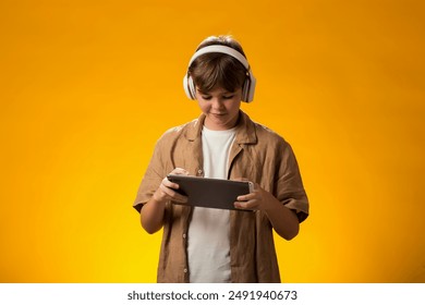 Portrait of boy using tablet and headphones and playing video game over yellow background. Leisure and gadget addiction concept. - Powered by Shutterstock