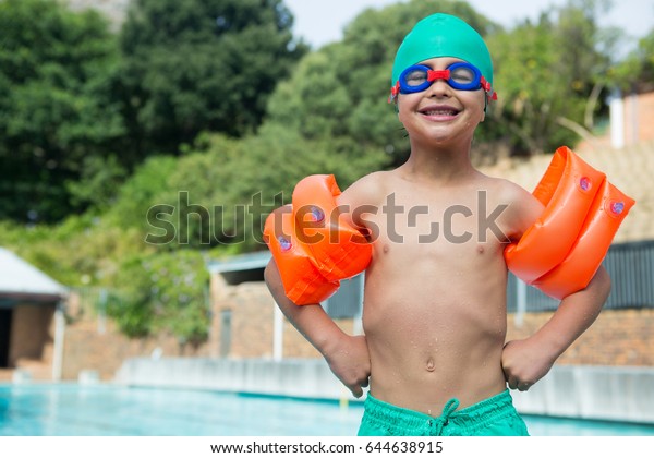 Portrait of
boy wearing arm band standing at
poolside