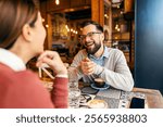 Portrait of a boyfriend sitting across the table with his female partner on blind date, flirting and smiling at her.