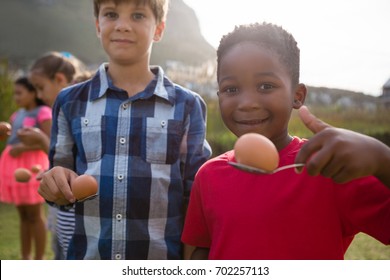 Portrait of boys playing egg and spoon race while standing in yard during party - Powered by Shutterstock