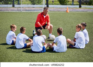 Portrait of boys team sitting in front of coach on football field listening to pre game lecture - Powered by Shutterstock