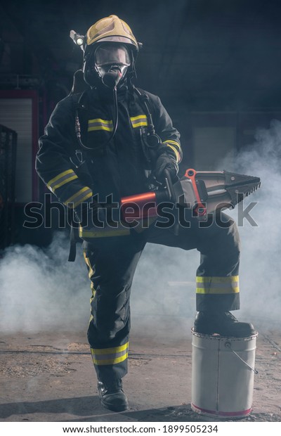 Portrait of a brave firefighter standing confident\
wearing full protective equipment, turnouts and helmet. Dark\
background with smoke and blue\
light.