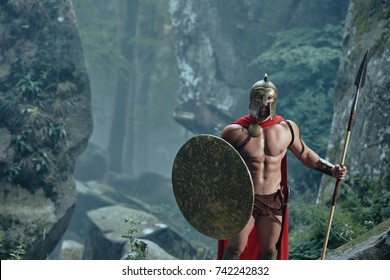 Portrait Of A Brave Spartan Warrior With Stunning Hot Sexy Ripped Body Wearing Battledress Walking In Through Foggy Woods.
