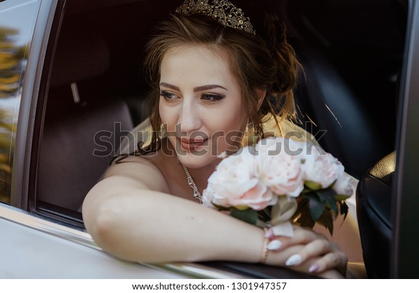 portrait of\
a bride in a car with a bouquet of\
roses.