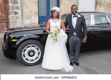 Portrait of bride and groom in front of luxury car