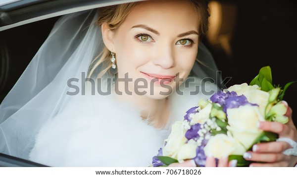 Portrait of the bride. The\
bride is holding a bouquet in the back seat of the car. Widescreen\
photo.