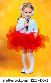 A Portrait Of A Bright Young Pretty Girl In Skirt With A Microphone. Fashion For Kids.