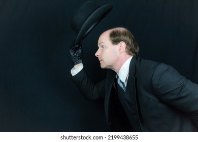 Portrait Of British Businessman In Black Suit And Leather Gloves Tipping Bowler Hat And Bowing In Polite Greeting. Classic English Gentleman Or British Butler.